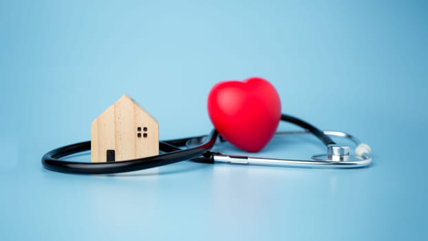 Concept of health insurance and medical welfare, small wooden house and red heart with stethoscope on blue background, health insurance and access to healthcare.