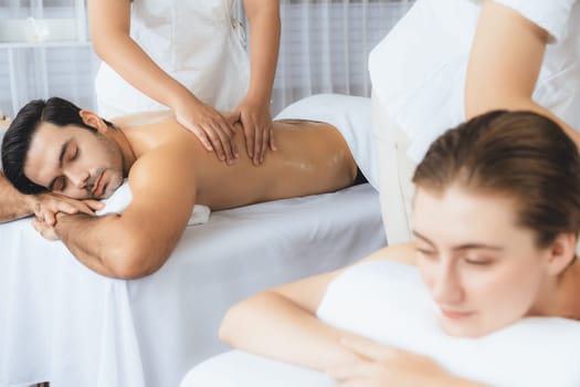 Caucasian couple customer enjoying relaxing anti-stress spa massage and pampering with beauty skin recreation leisure in day light ambient salon spa at luxury resort or hotel. Quiescent