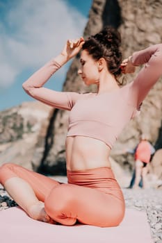 Young woman with long hair in white swimsuit and boho style braclets practicing outdoors on yoga mat by the sea on a sunset. Women's yoga fitness routine. Healthy lifestyle, harmony and meditation