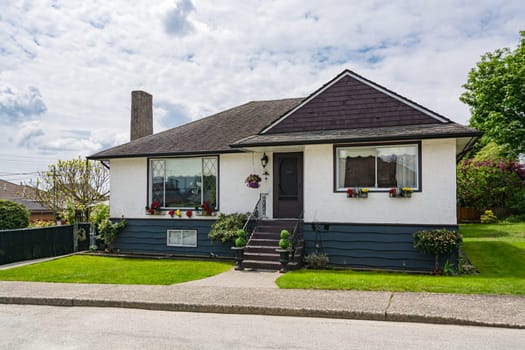 Small family house with green lawn in front. Average residential house on cloudy day in British Columbia