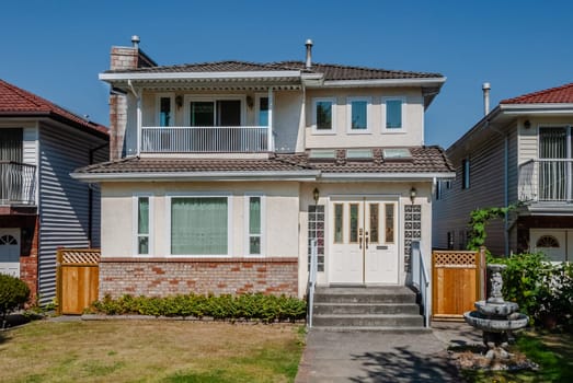 Average residential house with concrete pathway over the front yard on bright sunny day in British Columbia