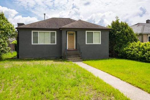 Modest family house with green lawn in front. Old residential house on sunny day in Canada