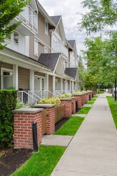 Row of townhouses with concrete pathway in front. Residential townhouses on cloudy day in Vancouver