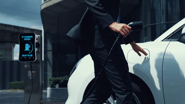 Businessman recharge his electric car from charging station at city center or public car park. Eco friendly rechargeable car using alternative clean energy in urban city lifestyle.Peruse