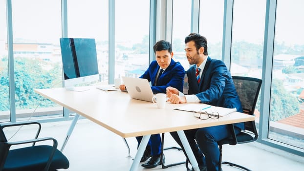 Two business people talk project strategy at office meeting room. Businessman discuss project planning with colleague at modern workplace while having conversation and advice on financial report. Jivy