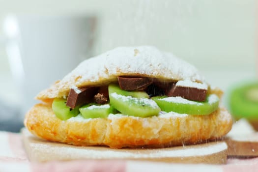 Sweet croissant with kiwi ricotta, chocolate close-up. Selective focus, delicious breakfast. Sprinkled with powdered sugar