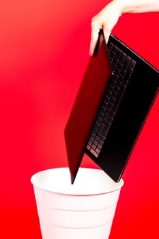 Black laptop in a trash bin on red background isolated