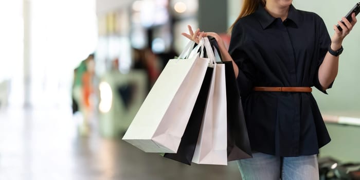 Woman using smartphone holding Black Friday shopping bag while standing on the side with the mall.