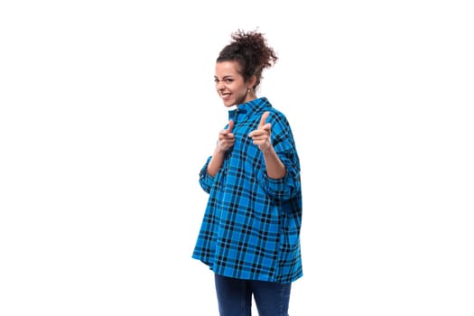 european young lady with curly ponytail hairstyle dressed in a blue shirt points her hand at the camera.