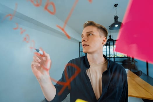 Professional caucasian businessman writing marketing idea by using mind map and sticky notes on glass board at modern meeting room. Creative business and planing concept. Closeup. Immaculate.