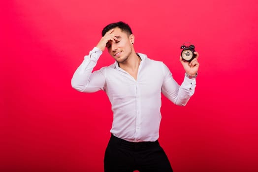 Emotional young man holding clock on a red background. Being late concept