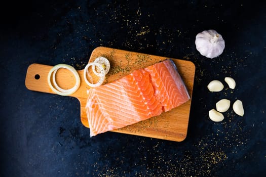 Raw salmon filet with rosemary and spices on a plate, black stone background. Top view, flat lay