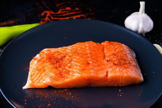 Raw salmon filet with rosemary and spices on a plate, black stone background. Top view, flat lay