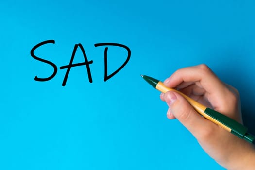 Children hand with pen write on a blue white background. Writing hand. Word SAD