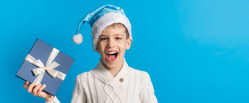 Child boy gift. Kid in blue christmas hat holds gift box. Shopping time. Banner header with copy space.