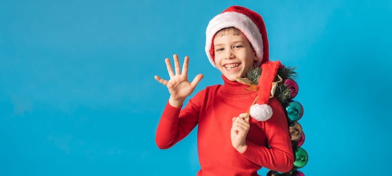 Cheerful child in santa hat hold christmas decorative balls on blue background, Xmas and holidays concept mockup. Generation alpha and gen alpha children