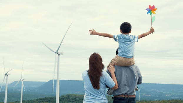 Concept of progressive happy family enjoying their time at the wind turbine farm. Electric generator from wind by wind turbine generator on the country side with hill and mountain on the horizon.