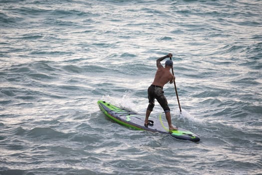 athletic wiry surfer guy swims with a paddle on a sup board in the sea Stand up paddleboarding