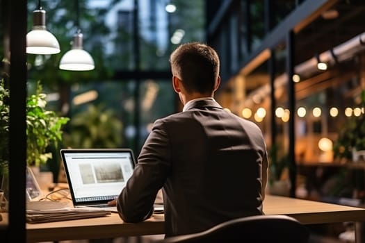 A man in a business suit works at a laptop in a modern office with large panoramic windows.