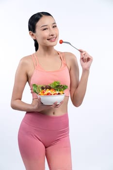 Young sporty Asian woman in sportswear holding salad bowl fill with vibrant of fruit and vegetable. Natural youthful and fit body lifestyle with balance nutrition on isolated background. Vigorous