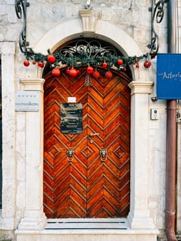 Garlanded wooden door to an old building with a sign at the entrance. Caption: Boutique Hotel, Astoria. High quality photo