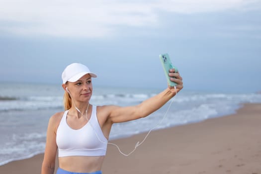 girl runner runs along the beach in sportswear. girl takes a selfie on the seashore before jogging. High quality photo