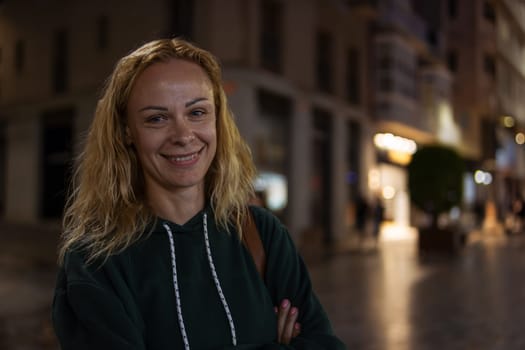 portrait of a smiling girl with blond hair in a green jacket, the girl stands on the street in the evening in the city, there is a place for an inscription. High quality photo