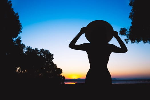 silhouette of a girl in a dress and hat at sunset on the sea the girl looks at the sunset, there is a place for an inscription. High quality photo