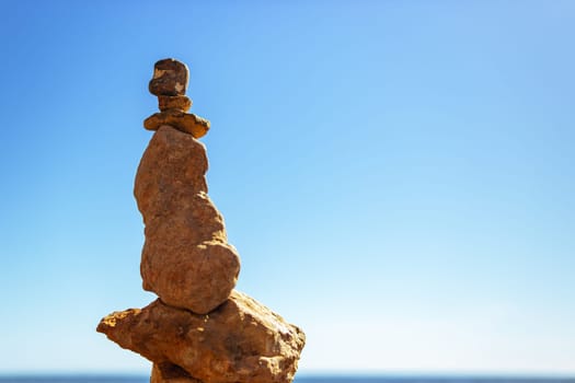 A pyramid of sea pebbles on a sunny sandy beach against a blue sky. The concept of life balance and harmony on the right there is space for an inscription. High quality photo