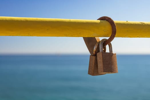 two locks are fixed on a yellow pipe against the background of the blue sea and sky. love and friendship concept. two locks are fixed on a yellow pipe against the background of the blue sea and sky. love and friendship conceptHigh quality photo
