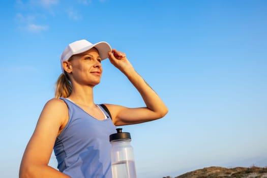 a girl in sportswear in a white cap and a blue T-shirt stands on the street against the blue sky and looks into the distance, there is a place for an inscription. High quality photo