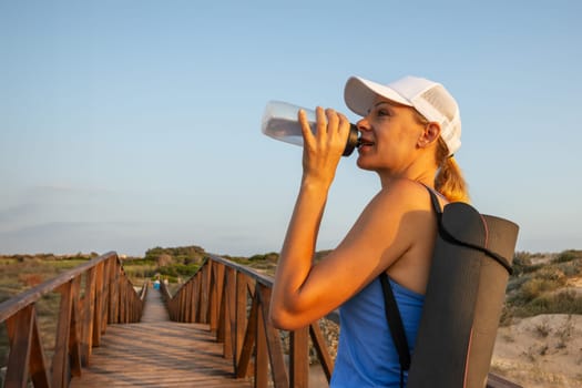 A sports girl stands drinking water from a bottle after a morning workout. High quality photo