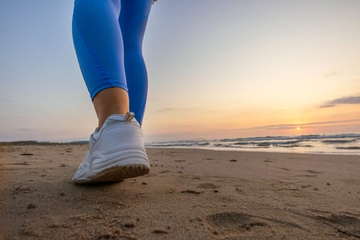 legs of a girl in blue leggings and sneakers running along the beach at dawn with space for inscription. High quality photo