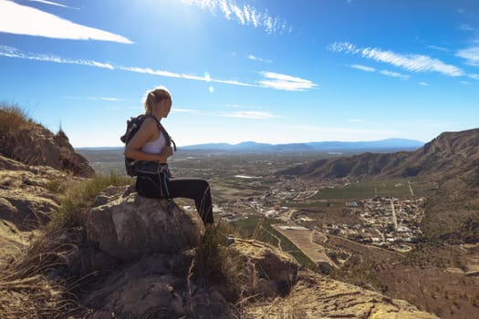 a girl in sportswear with a backpack sits on the mountain admiring the views. Hiking concept. High quality photo
