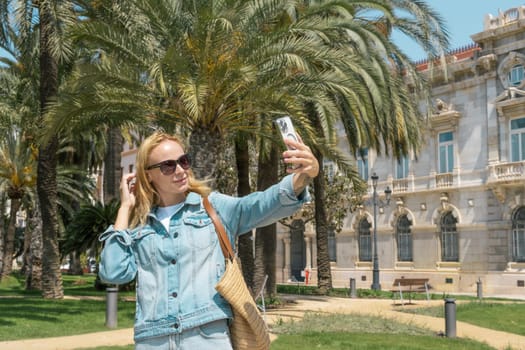portrait of a happy girl taking a selfie against the background of palm trees in the city, the concept of recreation and tourism. High quality photo
