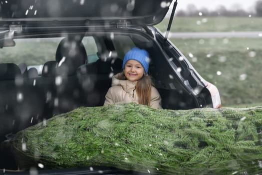 A girl sitting in the trunk with a Christmas tree