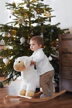 Boy rides a sheep near the Christmas tree at home