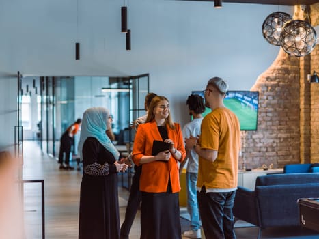 A group of young business colleagues, including a woman in a hijab, stands united in the modern corridor of a spacious startup coworking center, representing diversity and collaborative spirit.