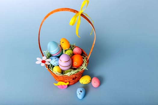 Top view of wicker basket filled with decorative multi colored easters eggs on a light blue background.
