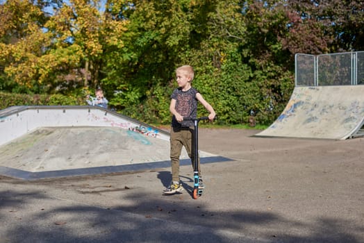 Child on kick scooter in park. Kids learn to skate roller board. Little boy skating on sunny summer day. Outdoor activity for children on safe residential street. Active sport for preschool kid. boy kid Roller park