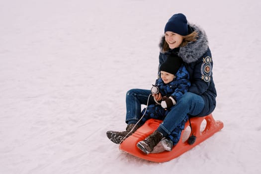 Laughing mother with a little boy rides a sled down the mountain. High quality photo