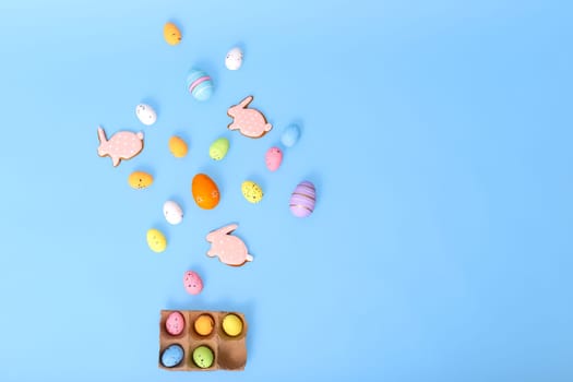decorative multicolored eggs and pink gingerbread in the form of rabbit, scattered on a light blue background, top view. Copy space