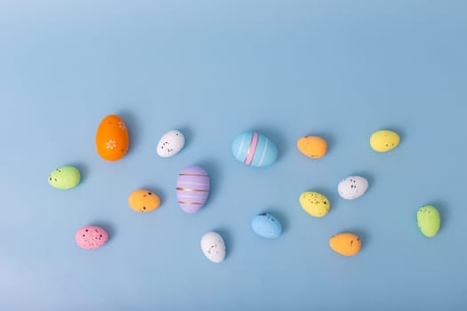 decorative multicolored eggs are scattered on a light blue background, top view.