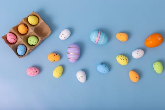Beautiful decorative multicolored eggs are scattered on a light blue background, top view.
