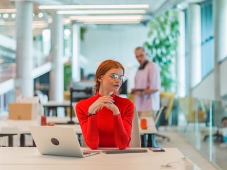 In a modern startup office, a professional businesswoman with orange hair sitting at her laptop, epitomizing innovation and productivity in her contemporary workspace.