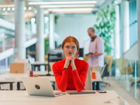 In a modern startup office, a professional businesswoman with orange hair sitting at her laptop, epitomizing innovation and productivity in her contemporary workspace.