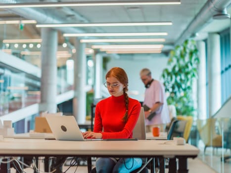 In a modern startup office, a professional businesswoman with orange hair sitting at her laptop, epitomizing innovation and productivity in her contemporary workspace.