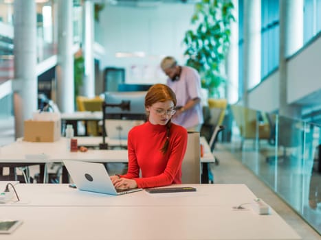 In a modern startup office, a professional businesswoman with orange hair sitting at her laptop, epitomizing innovation and productivity in her contemporary workspace.