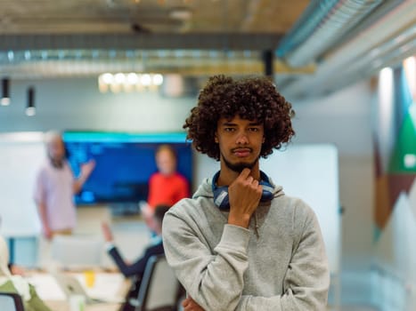 In a modern office environment, an African American young entrepreneur with headphones engages in work, while in the background, his dedicated colleagues exemplify teamwork and collaboration, encapsulating the essence of contemporary corporate success.