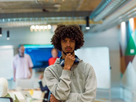 In a modern office environment, an African American young entrepreneur with headphones engages in work, while in the background, his dedicated colleagues exemplify teamwork and collaboration, encapsulating the essence of contemporary corporate success.